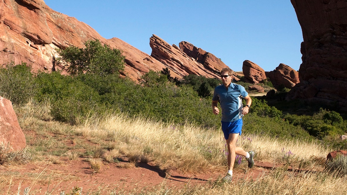 In the morning, a man runs down a trail ringing Red Rocks Park and ampitheater past sandstone fountain formations.