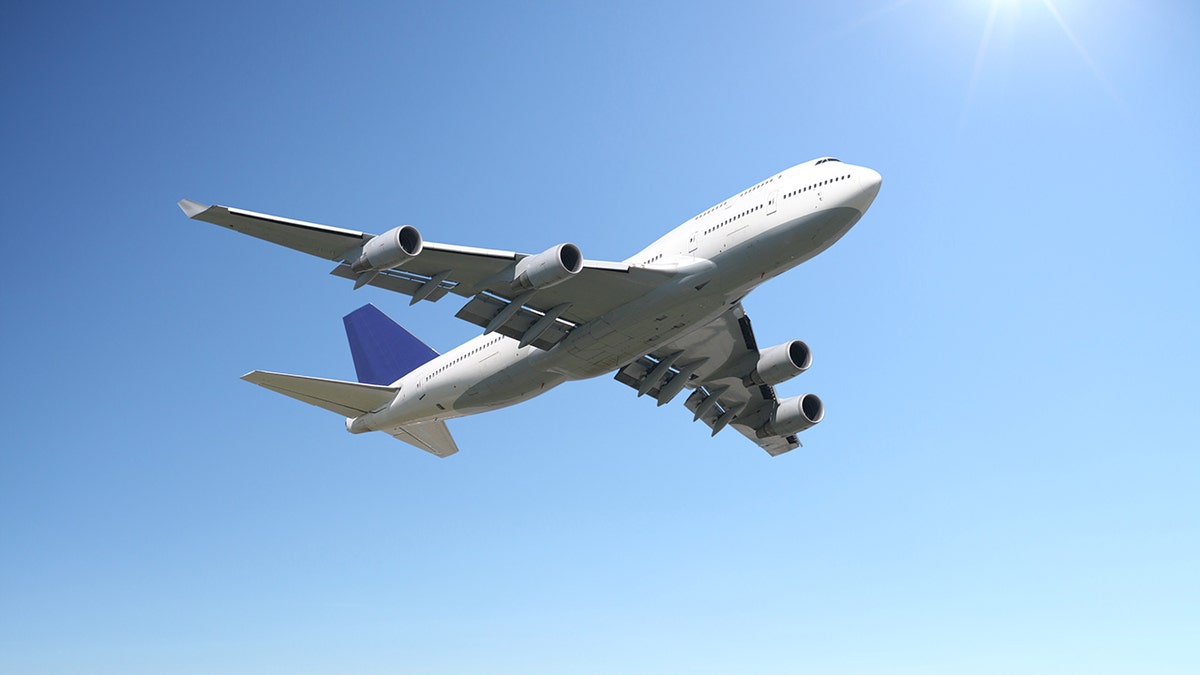 Large commercial jet airplane flying overhead against a clear blue sky on a sunny day.