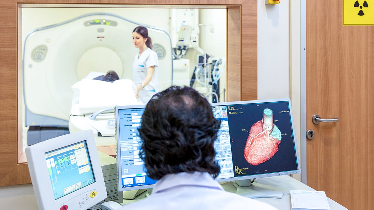 doctor watches over screens while patient lays down in heart scan