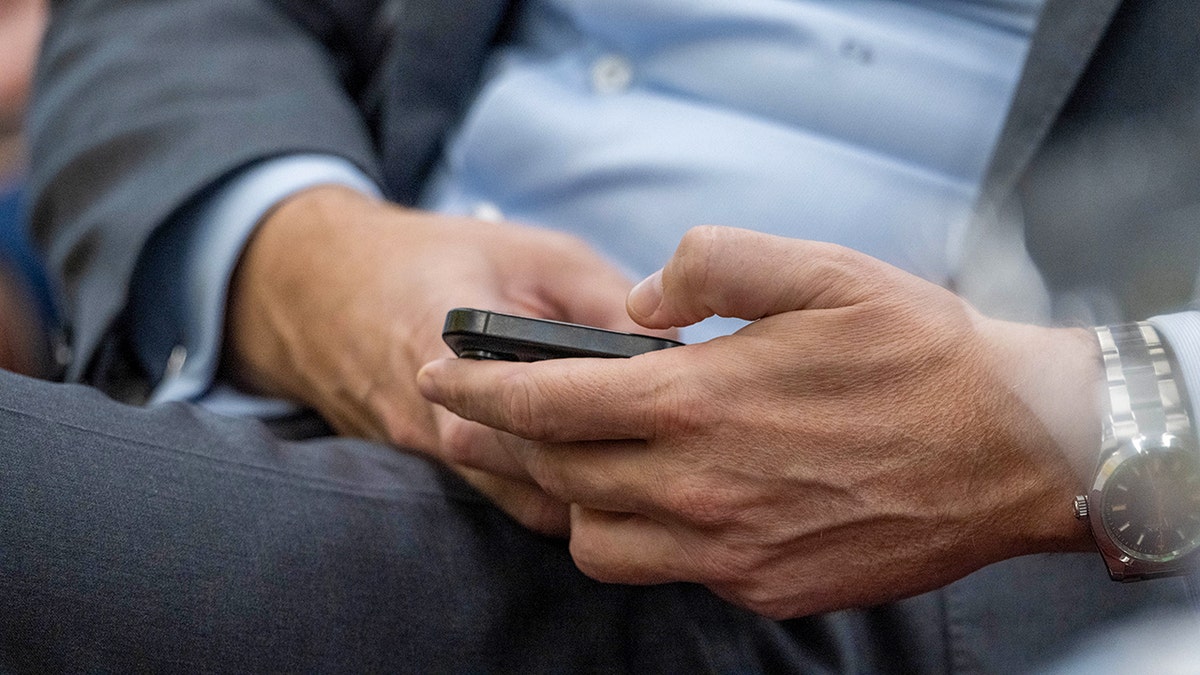 Man in a suit typing on his phone.