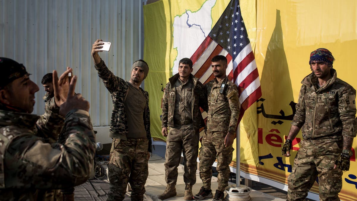 Syrian Democratic Forces (SDF) fighters pose for a photo with the American flag on stage after a SDF victory ceremony announcing the defeat of ISIL in Baghouz was held at Omer Oil Field on March 23, 2019 in Baghouz, Syria.
