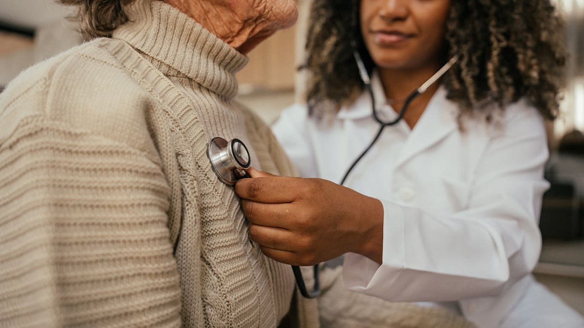 Healthcare professional listening to elderly woman's heart with stethoscope at home