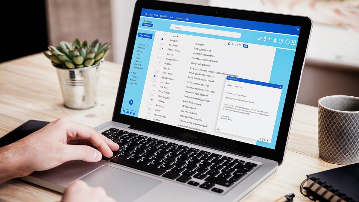 A laptop sitting on a desk shows an email inbox on its screen.