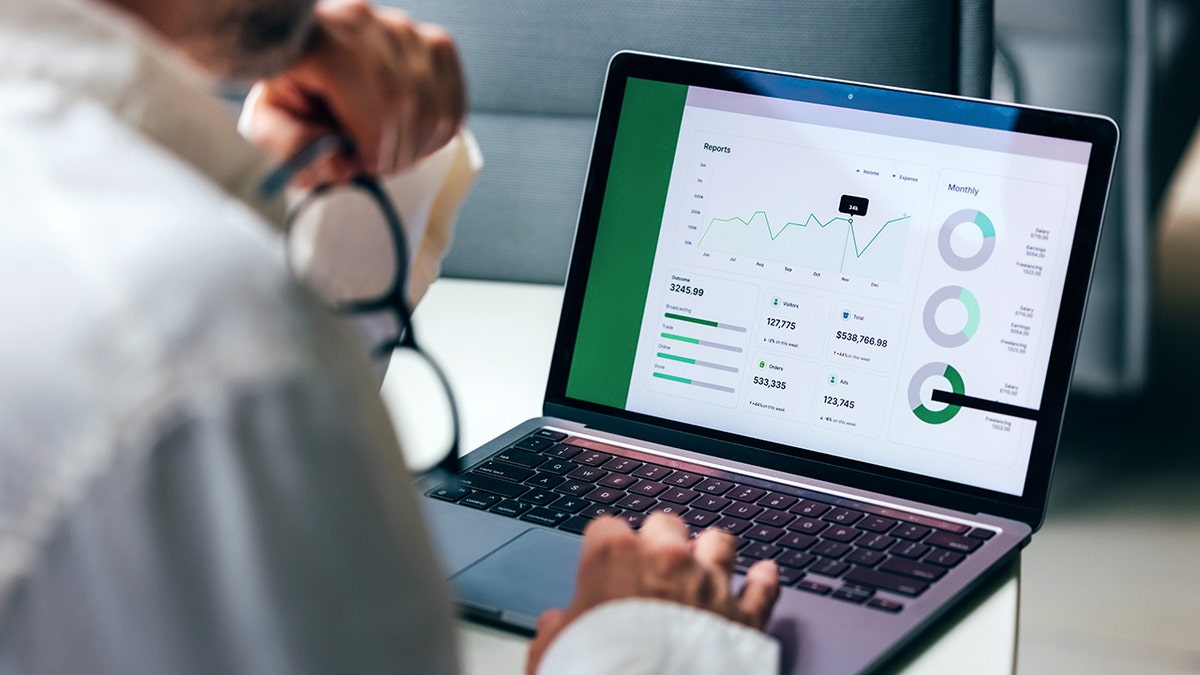 A person holds their glasses to the side as they look at data on a laptop screen.